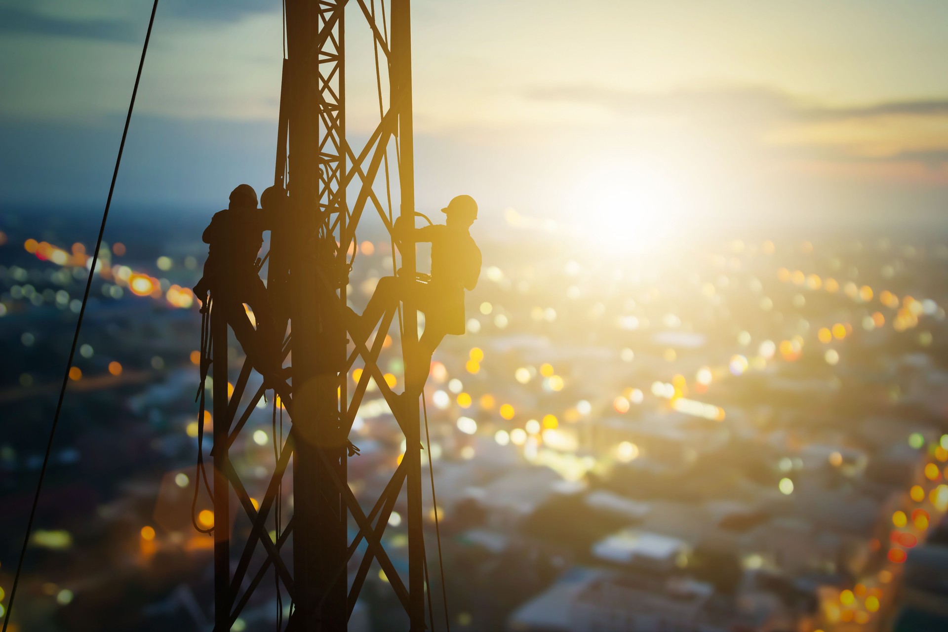 Silhouette electrician work on high ground heavy industry concept. Construction of the extension of high voltage in high voltage stations safely and systematically over blurred city background.